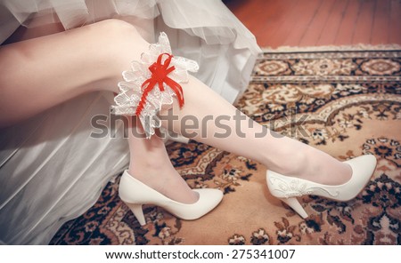 bride dresses garter on the leg. Picture of beautiful female barefoot legs in wedding dress.