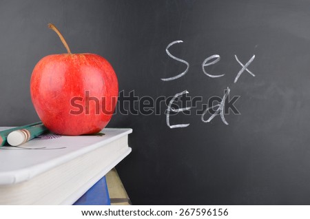 Classroom with red apple,books and handwriting in white chalk on blackboard saying sex education