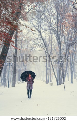 Girl with umbrella walking on the path. Winter. Trees with red leafs.