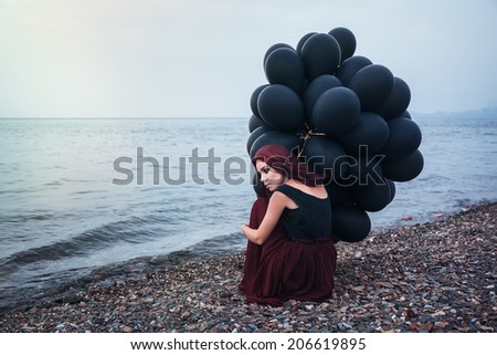 Beautiful girl walking in the beach while holding black balloons