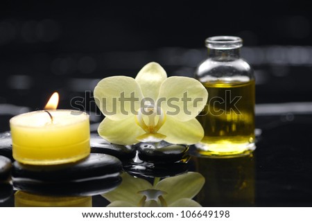 bottle of essential oil and yellow orchid with candle on pebble