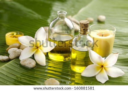 Two frangipani and stones with yellow candle ,massage oil on wet banana leaf