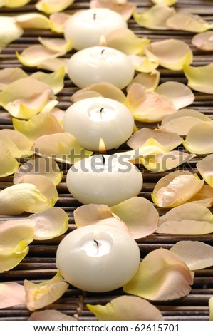 A line of white candle and rose petals on mat