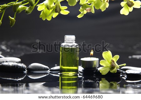 tranquil spa scene - massage oil and candle on black stones with green orchid