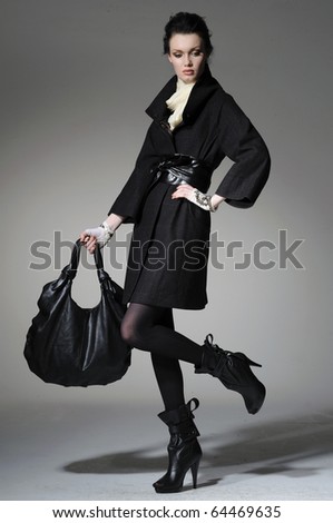 High fashion model in winter fur coat clothes with bag posing in the studio