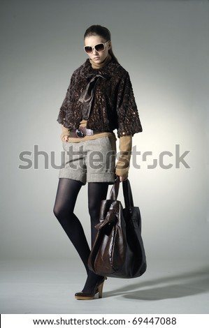 fashion model in autumn/winter clothes holding handbag posing in light background