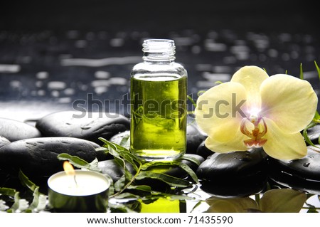 tranquil spa scene - massage oil and candle with black stones with green orchid