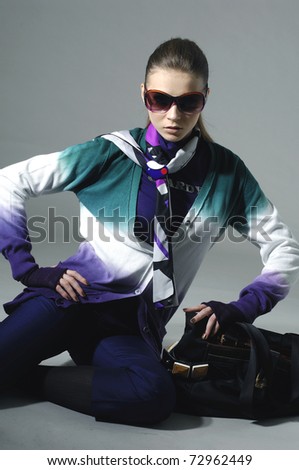 High fashion model in fashion clothes wearing sunglasses sitting in the studio
