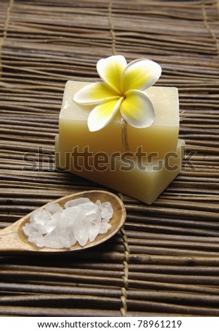 Frangipani flower with bath salt in wooden spoon and soap on mat