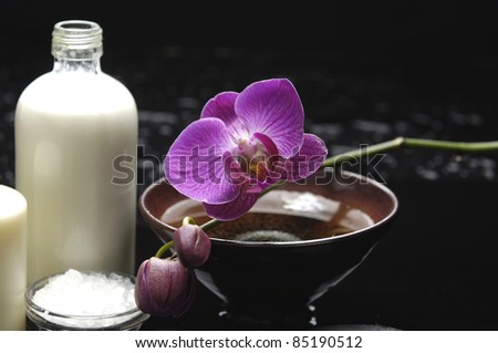 bottle of massage oil and orchid in bowl with bath salt in bowl on black