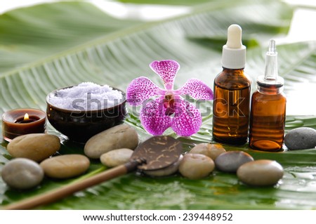 spa supplies with orchid, oil, candle , salt in bowl, spoon ,stones on banana leaf