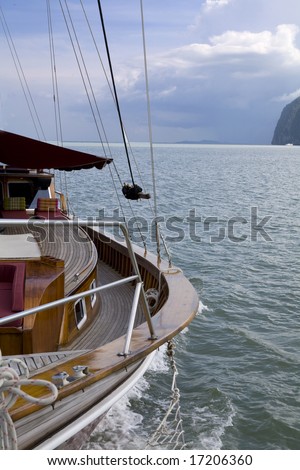 A wooden yacht sailing on the ocean with a storm in the background