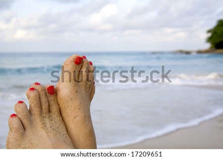 A woman's sandy feet with red nail polish on the beach