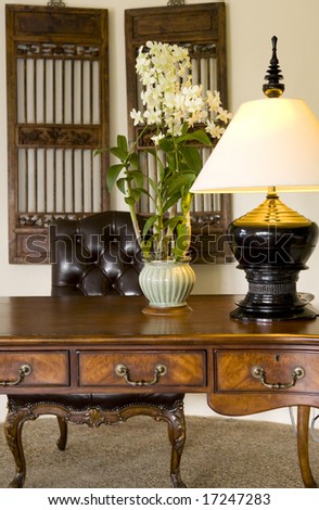 An antique writing desk and leather chair with decorated with a lamp and flowers
