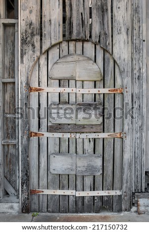 Old grey rusty abandoned unused driftwood wooden arched double door with holes and gaps weathered by beach