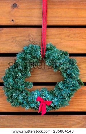 Green fir Christmas wreath with small red bow handing on wooden planks