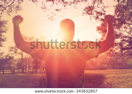 Successful happy accomplished man stands with raised arms facing the sun. White male athlete with arms up celebrating and happy with his achievement and exercise.