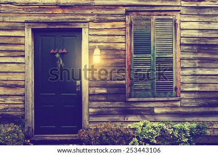 Old rustic vintage antique dilapidated house home building structure cottage with green intricate front door and window with shutters closed shut and porch light lantern glowing turned on