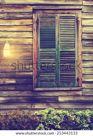 Old rustic vintage antique dilapidated run down leaning house home building structure with green closed shut shutters over window and porch light lantern glowing turned on