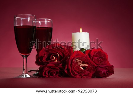bouquet of red roses, two glasses of wine and a candle on red background