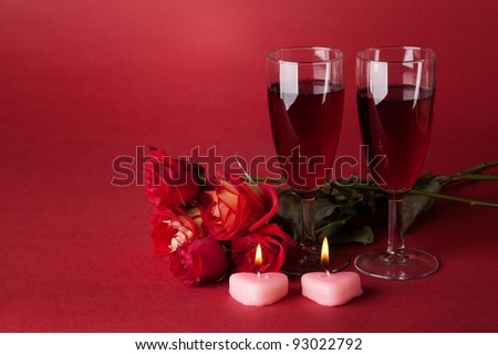 bouquet of red roses, two candles and two glasses of wine on a red background