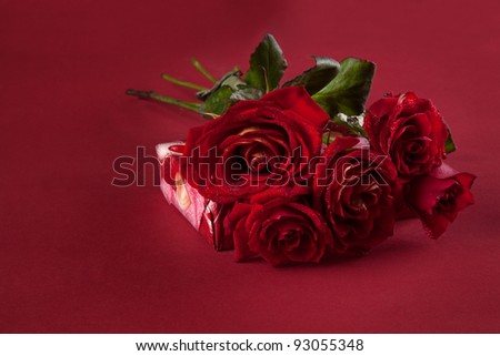bouquet of red roses and a gift for Valentine\'s Day on a red background