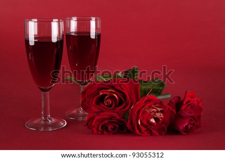bouquet of red roses and two glasses of wine on a red background