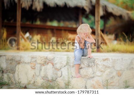 Cute little girl sitting on the curb in the summer near the beach bar
