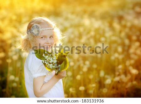 Cute little girl standing in a field and smiling. Portrait, joy, smile, dandelions, lily of the valley.