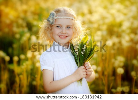 Cute little girl standing in a field and smiling. Portrait, joy, smile, dandelions, lily of the valley.