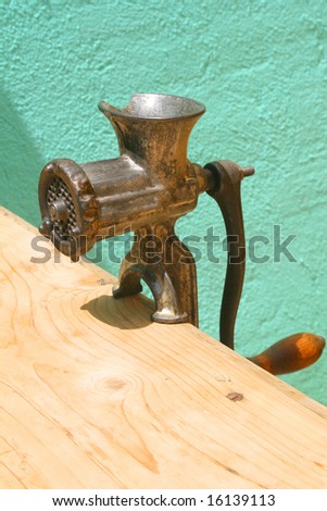 Antique meat grinder on weathered wooden table against turquoise wall