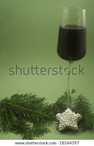 A glass of red wine and single star cookie with fir branch isolated on green paper