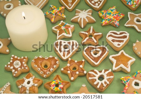 White pillar candle surrounded by decorated gingerbread cookies on green background