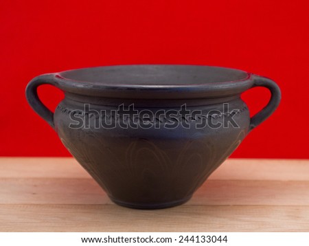 Black clay pot on the wooden floor against red background