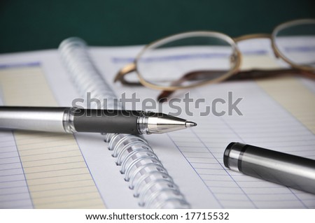 Business Books, Charts, Expenses, Bookkeeping, Pen w/ Glasses on top of spiral bound monthly accounting income and expense reports.