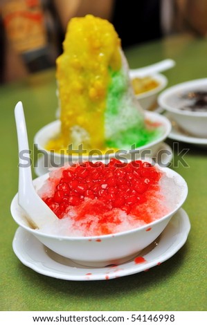 Bowl of ice kacang (red bean) dessert with mango and corn topping, and red ruby dessert
