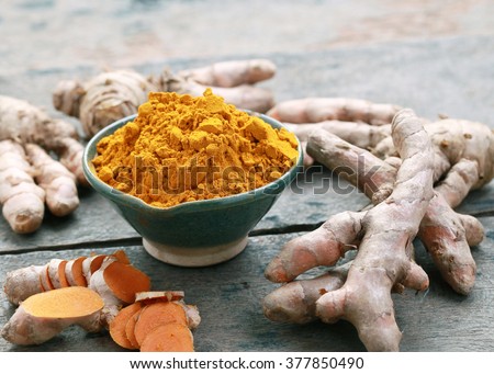 Turmeric powder and turmeric on wooden background.