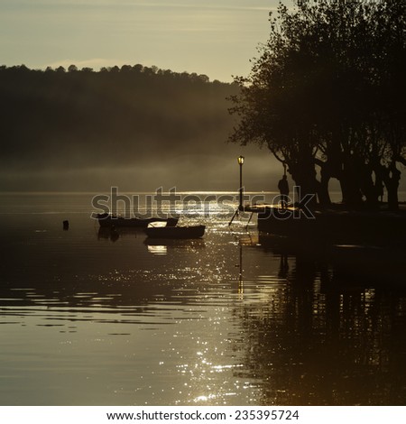 man walking in misty lake with boats