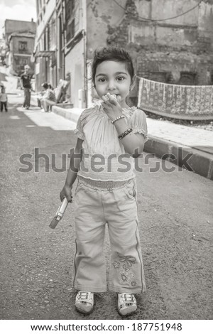 ISTANBUL, TURKEY - MAY 20, 2011: A baby girl holds her pacifier, as she plays with her toy gun in a neighborhood of Istanbul, in the Fener district. A poor district of the city.