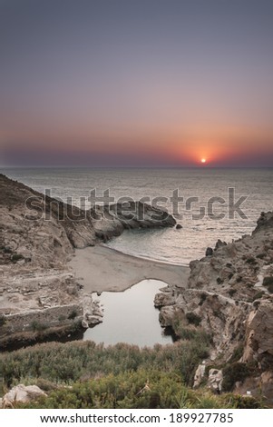 A sandy beach, with a river ending at the sea, and the ruins of an ancient temple of goddess Artemis, located in Ikaria island, Greece, during sunset.