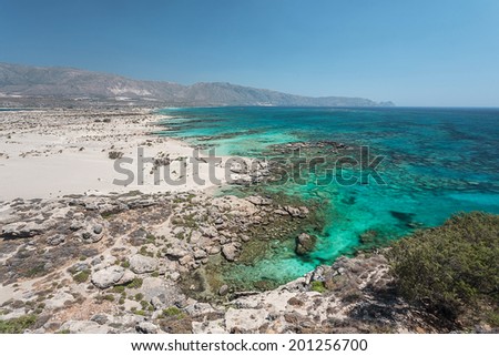View of the Elafonisi beach, with some rocks inside a crystal clear, turquoise calm water, and a clear blue sky, during summer time, in the daylight, located in the island of Crete, Greece.