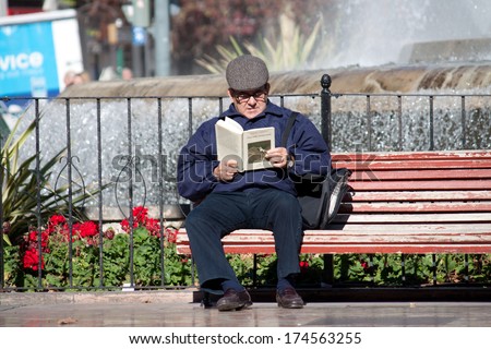 VALENCIA, SPAIN - JANUARY 27, 2014: A senior man reads a book on a park bench near the city center of Valencia, Spain.