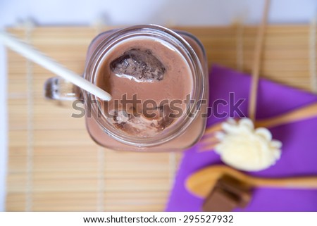 Ice chocolate drink in big glass and chocolate bar in wooden spoon