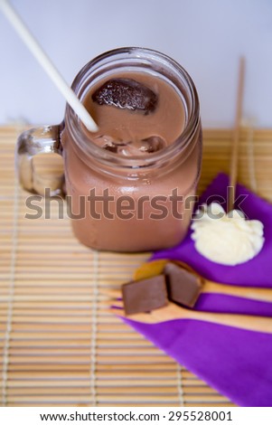 Ice chocolate drink in big glass and chocolate bar in wooden spoon