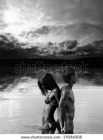 Man and woman are standing back to back in water / black and white photo