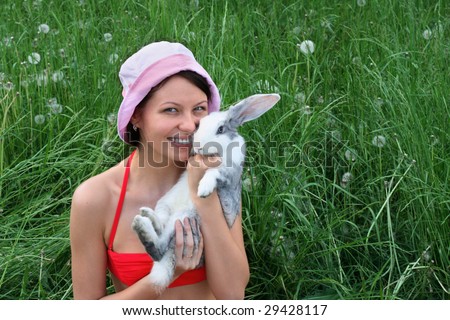 A young smiling woman sitting on the grass holds a rabbit