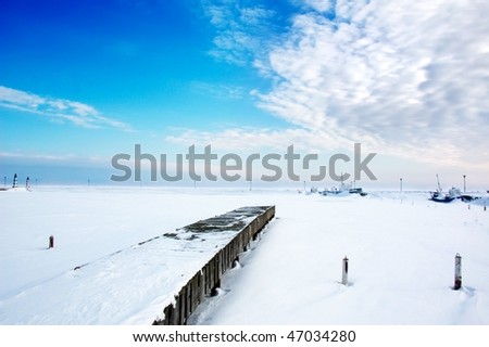 winter landscape with snow covered ice, boats and pier, under blue sky