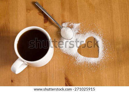 Cup of  black coffee, spoonful of sugar and heart shape out of granulated sugar on wooden table