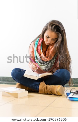 Young woman sitting on the floor and reading a book for the university