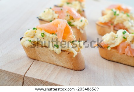 Toast with smoked salmon with scrambled eggs on wood plate